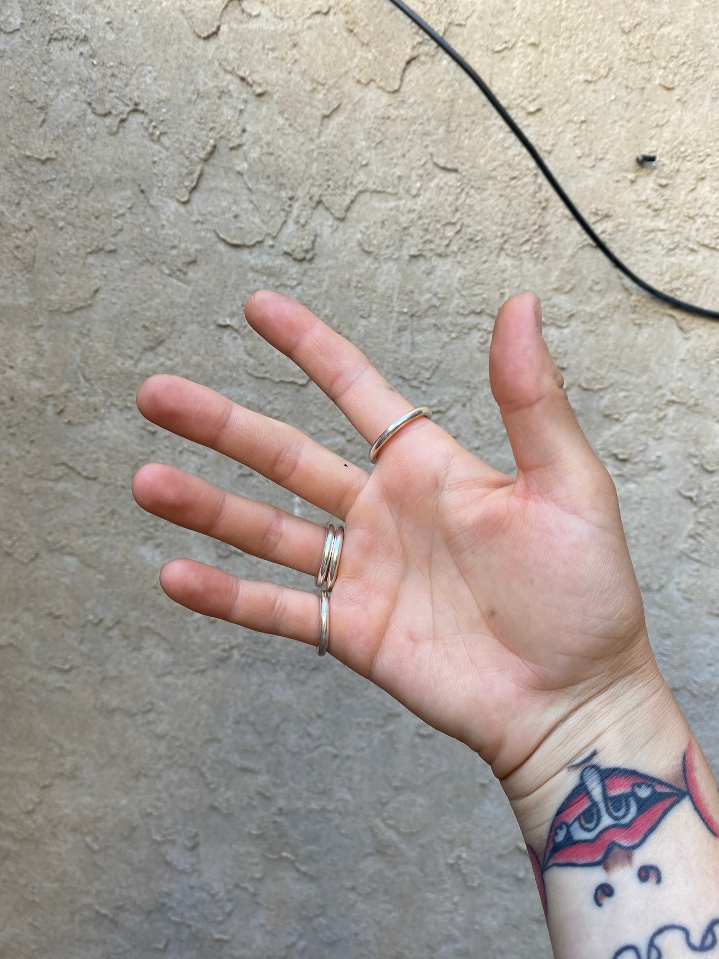 Chunky round sterling silver rings stacked on someone's right hand infront of a wall.
