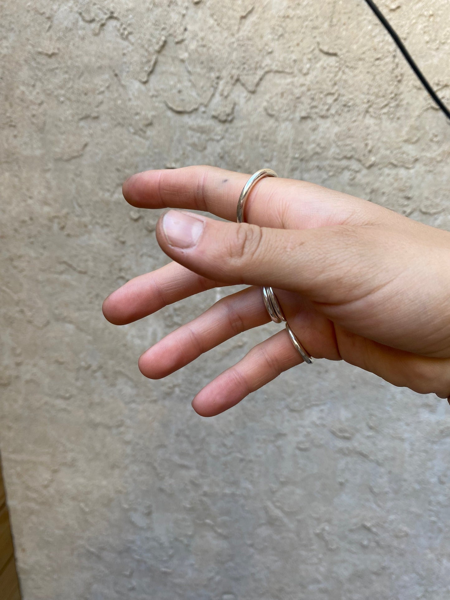 Chunky round sterling silver rings stacked on someone's right hand infront of a wall.