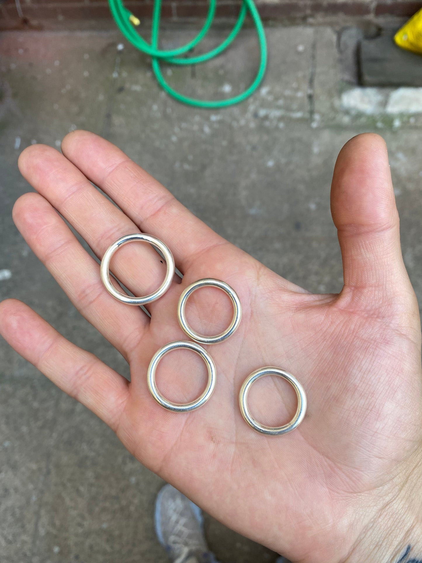 Chunky round sterling silver rings placed in someone's right palm over the floor.