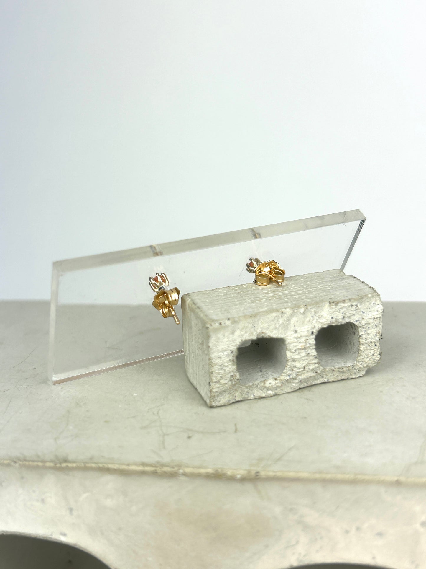 Back view 14k gold earrings with bright orange carnelians, showing the earring backs and are displayed on a clear acrylic card held up by a miniature cinderblock infront of a white background.