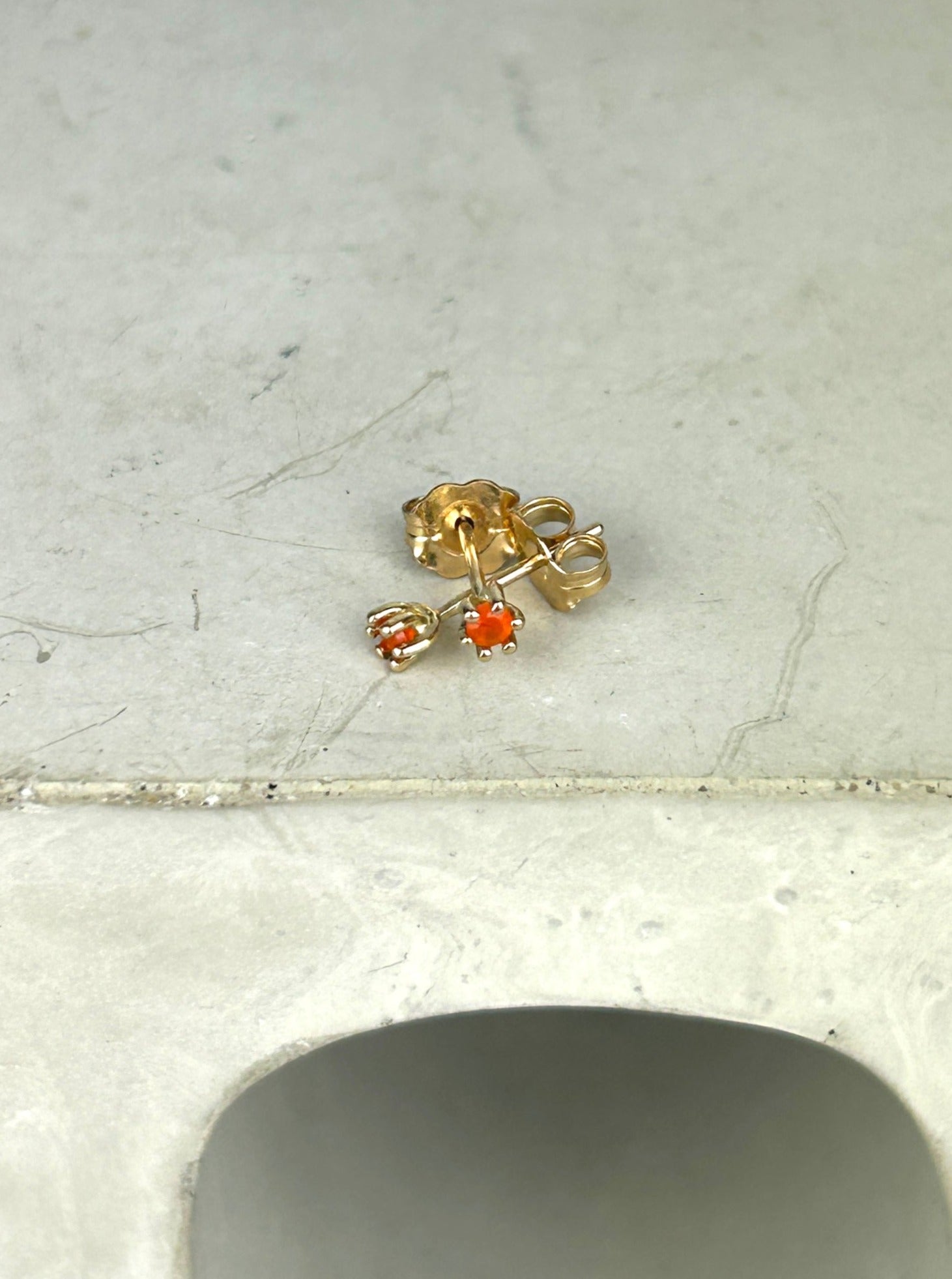 Top view of 14k gold earrings with bright orange carnelians that resemble tulips are laid in a criss crossing pattern on a grey surface