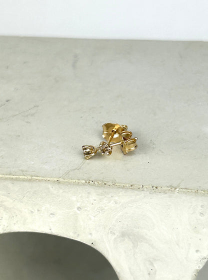Top view 14k yellow gold stud earrings holding 2mm round cut smoky quartz laying in a criss cross pattern on a smooth grey surface.