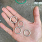 Chunky round sterling silver rings placed in someone's right palm over the floor.
