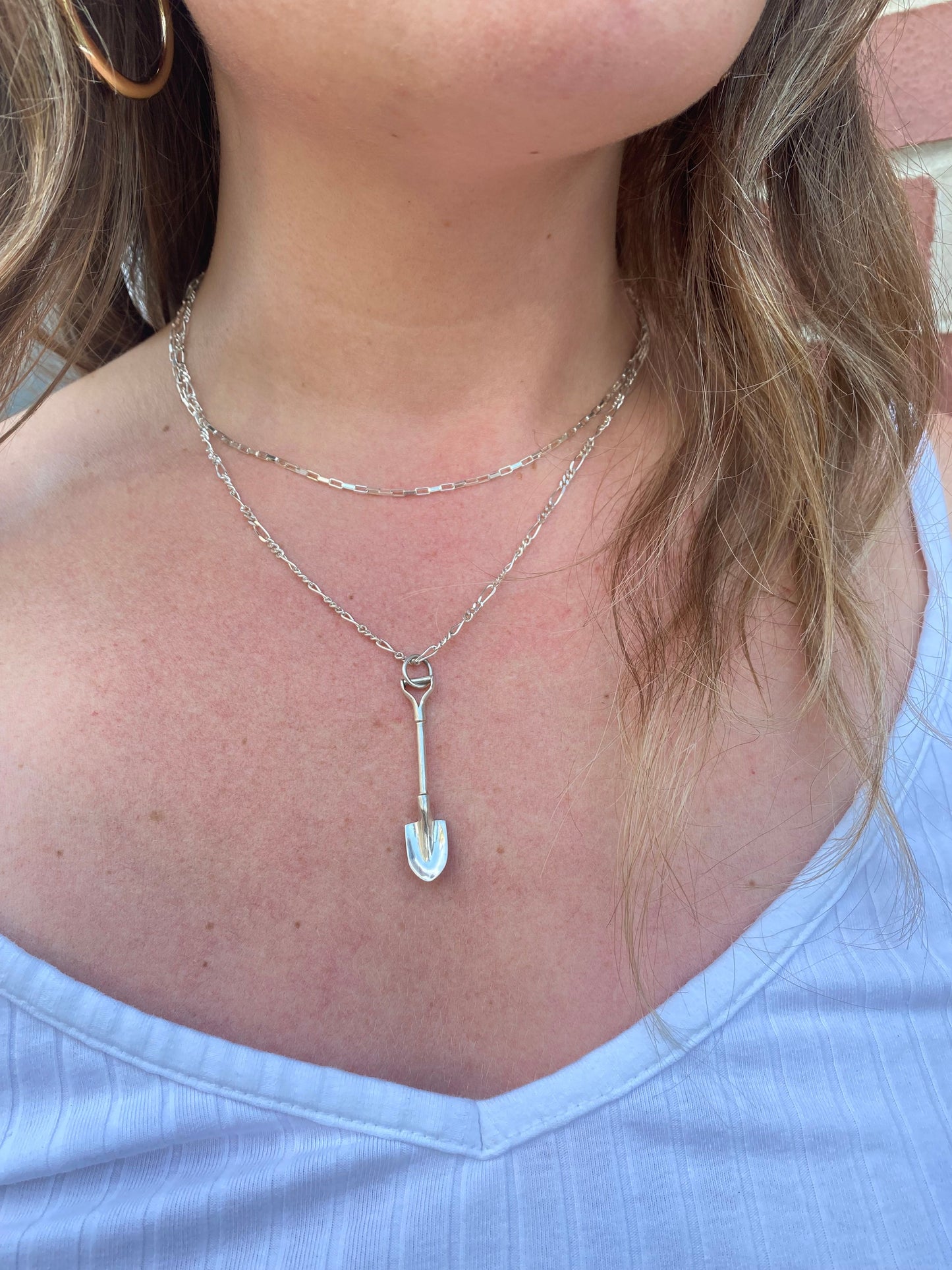 Mini sterling silver shovel hangs on an 18" silver figaro chain. Pictured on a model's chest.