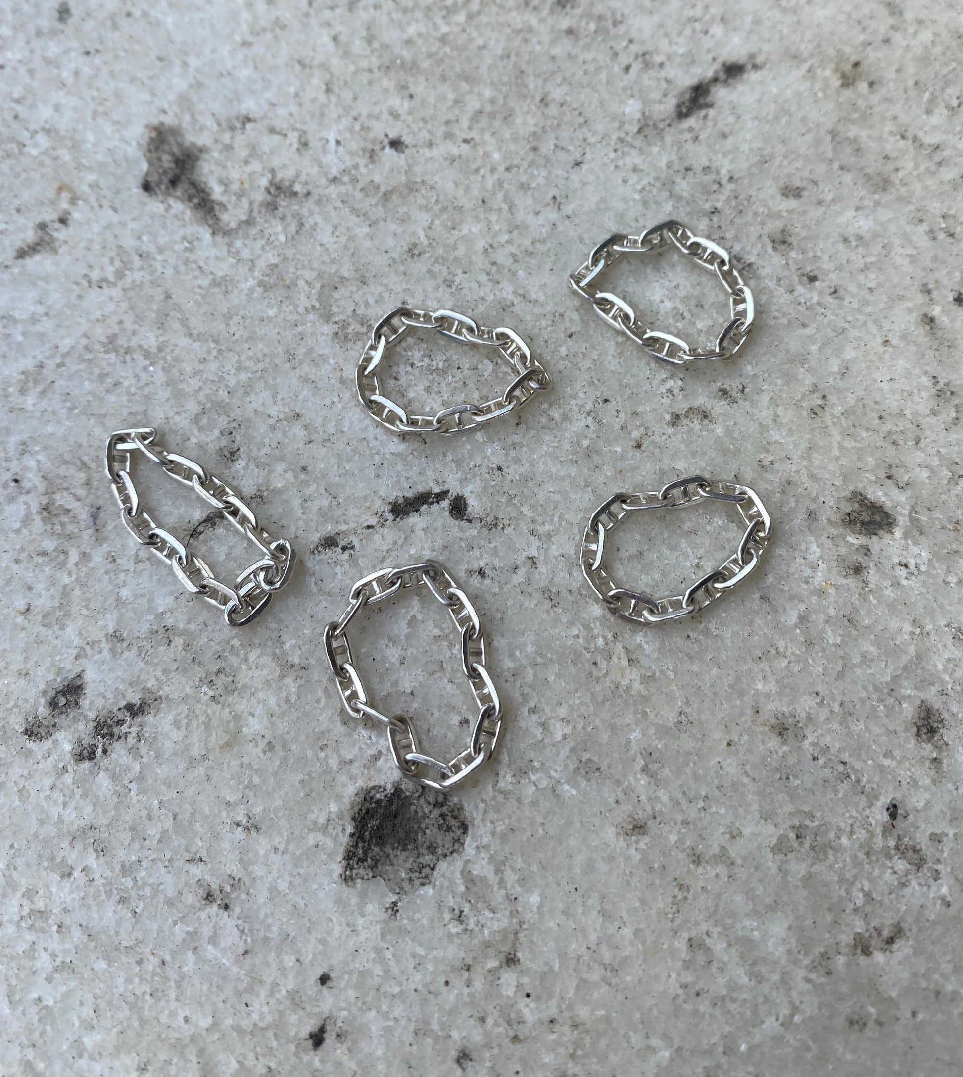 Sterling silver loose chain link rings scattered on a piece of marble.